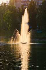 Picturesque landscape view of pond with fountain during sunset. Fountain in the city channel.  Buildings of famous Rusanivka neighborhood in the background. Kyiv, Ukraine