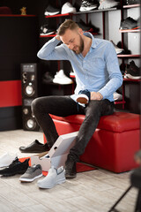 caucasian bearded man chooses hiking shoes while sitting in fitting room of modern sports store....