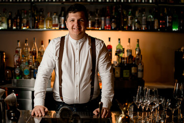 young smiling bartender in a white shirt stands at the bar counter.
