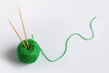 Green yarn thread with knitting needles on a gray background for knitting.
