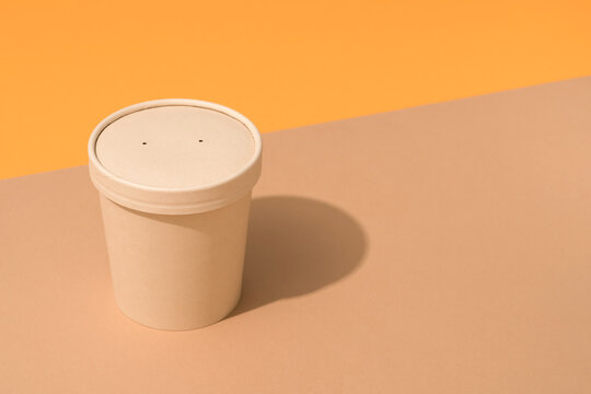 Brown Disposable Kraft Paper Container With Paper Caps For Soup Or Beverages Over Light Brown And Orange Background, Mockup Image. Sustainable Street Food Packaging Concept