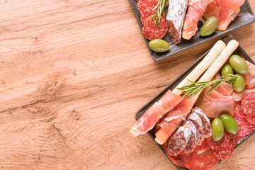 Assortment of different meat snacks, charcuterie plates with several types of sausages - proscuitto served with olives. Black plates with traditional italian antipasti on wooden table with copy space