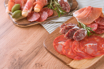 Various meat snacks, charcuterie board with several types of sausages - salami, bresaola, proscuitto served with olives. Wooden serving boards with traditional italian antipasti over wooden table