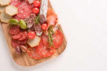 Wooden charcuterie board with different types of sausages - salami, bresaola, proscuitto served with olives. Traditional italian antipasti on white concrete table background with copy space