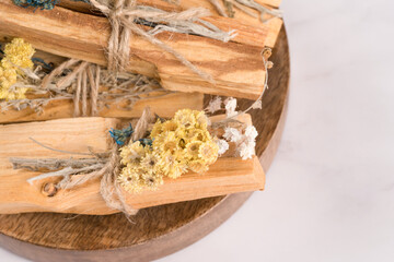 Holy wood sticks, incense for meditation and spiritual practices on white marble table background. Palo santo sticks with bouquets of dried flowers on wooden tray. Selective focus