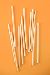 Natural wheat drinking straws made of the stem of the wheat plant on orange background. Sustainable lifestyle and zero waste concept. Ethical consumerism. Flat lay