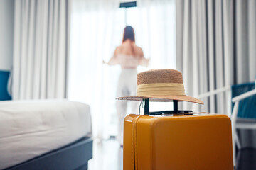 Close-up luggage with hat and blurred happy tourist woman background in hotel after check-in. Conceptual of travel and vacation. - obrazy, fototapety, plakaty