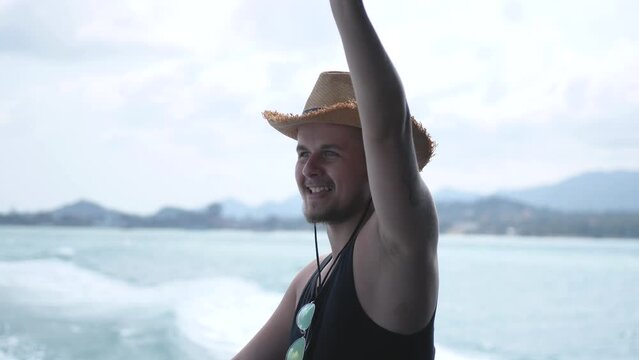 Young man in summer hat swimming on catamaran yacht and waving hand with sea water background. Summer holidays. Travel vacation. 3840x2160
