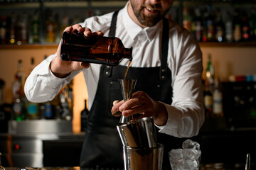 Close-up view of male bartender hands holding bottle and pours beverage into steel jigger