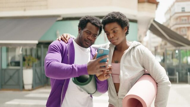 African american man and woman couple holding yoga mat making selfie by the smartphone at street