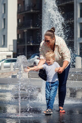 Mom and her son, in the city center, by a fountain of water. The child is afraid to touch the water...
