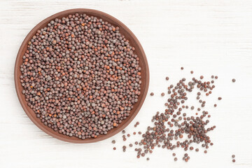Mustard in clay plate and scattered in a heap on white wooden background. Healthy eating concept