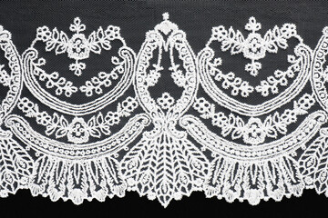 White lace with a beautiful pattern on black background isolated. Sewing and fabric concept