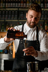 Close-up view of male bartender hands holding bottle and masterfully pours beverage into steel jigger