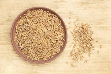 Spice cumin (jeera) in clay plate and bunch on brown wooden background. Vegetarian food concept