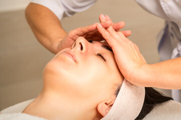 Obraz na płótnie Canvas Facial massage. Young caucasian woman with closed eyes getting a massage on her forehead in a beauty salon