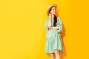 Young beautiful smiling female in trendy summer green dress. Sexy carefree woman posing near yellow wall in studio. Positive model having fun. Cheerful and happy. In hat. Isolated