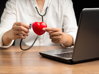 A doctor hand holding a stethoscope checking a red heart shape while sitting in the hospital or clinic