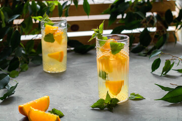 Two glasses with a refreshing orange drink. A type of lemonade. Mineral water with pieces of fresh orange and mint. Detox, diet. Behind the wooden lattice, entwined with greenery.