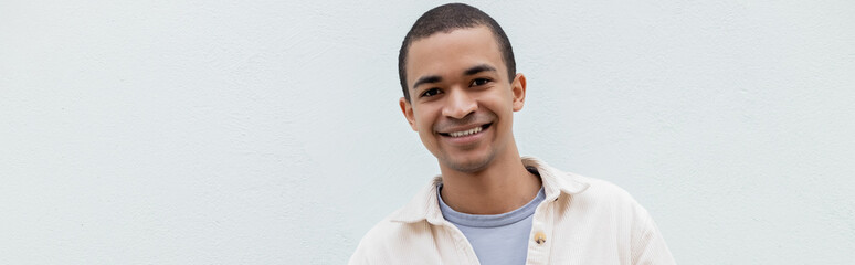 Obraz premium happy african american man smiling while looking at camera outside, banner.