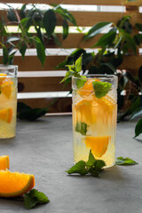 Refreshing orange drink. A type of lemonade. Mineral water with pieces of fresh orange and mint. Detox, diet. Behind is a wooden lattice entwined with greenery.