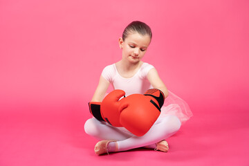Little classical dancer girl wearing boxing gloves isolated on pink background. Female stereotypes...
