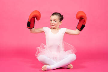 Little proud classical dancer girl showing biceps and wearing boxing gloves with funny face. Female stereotypes concept. - obrazy, fototapety, plakaty