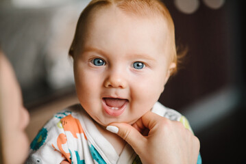 Baby boy portrait looking at camera. Close-up mother hands open baby mouth to examine first teeth....