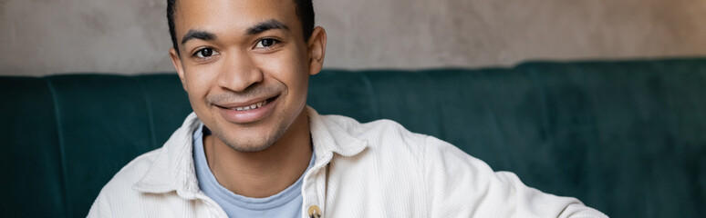 positive and young african american man looking at camera in coffee shop, banner.