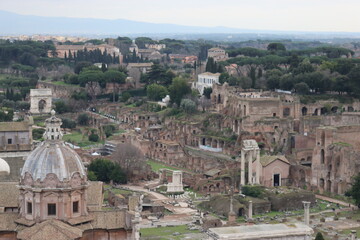 Fototapeta premium ROME, ITALY - February 05, 2022: Panoramic view around the Colosseum in city of Rome, Italy. Cold and gray sky in the background. Macro photography of the green parks with the old buildings.
