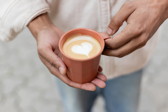 cropped view of african american man holding takeaway coffee drink with latte art in cup.