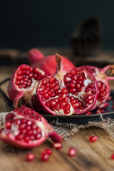 beautiful pomegranate fruits with pits on a metal plate on a wooden table in a dark key in rustic...