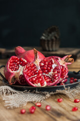 Obraz na płótnie Canvas beautiful pomegranate fruits with pits on a metal plate on a wooden table in a dark key in rustic style