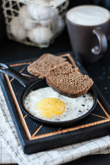 traditional breakfast - fried eggs in a cast-iron frying pan with black bread on a dark background