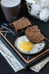 traditional breakfast - fried eggs in a cast-iron frying pan with black bread on a dark background