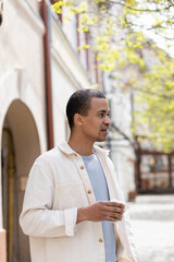 african american man in shirt jacket holding takeaway beverage in urban city.