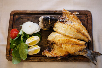 Grilled fried fish with vegetables and lemon on wooden cutting board.High angle, top view.Concept of dish in restaurant,sea food,table layout,healthy and tasty eating