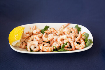 Shelled shrimps with lemon on white plate on blue table cloth.Seafood, delicacy dishes concept.Copyspace