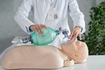 Close-up of medical worker in white coat demonstrating reanimation of patient on mannequin with oxygen mask