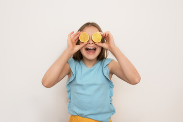 a little girl in a blue T-shirt holds lemon halves to her face and smiles happily stroking the camera, healthy eating, happy childhood,