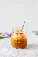 caramel sauce in a glass jar with a spoon inside on a light background