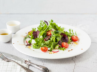 Green salad of fresh lettuce leaves, cherry tomatoes, feta cheese and assorted seeds with a sauce of honey, olive oil and balsamic vinegar on a flat plate on a stone table. Healthy vegan food.