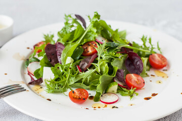 Green salad of fresh lettuce leaves, cherry tomatoes, feta cheese and assorted seeds with a sauce of honey, olive oil and balsamic vinegar on a flat plate on a stone table. Healthy vegan food.