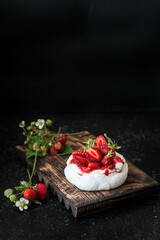 Dessert Pavlova with wild strawberries on a black background. Close-up of dessert with white cream and berries