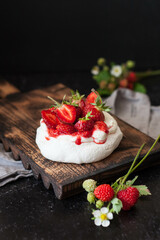 Dessert Pavlova with wild strawberries on a black background. Close-up of dessert with white cream and berries
