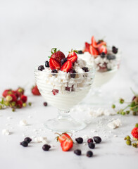 Pavlov air dessert with whipped cream, meringue and berries in a glass on the table close-up on a light background