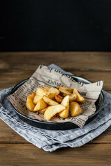 Delicious baked potatoes close-up on an old newspaper in a metal plate on a wooden table