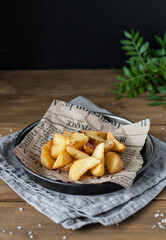 Delicious baked potatoes close-up on an old newspaper in a metal plate on a wooden table