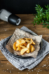 Delicious baked potatoes close-up on an old newspaper in a metal plate on a wooden table