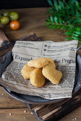 Chicken nuggets close-up on an old newspaper in a metal plate on a wooden table